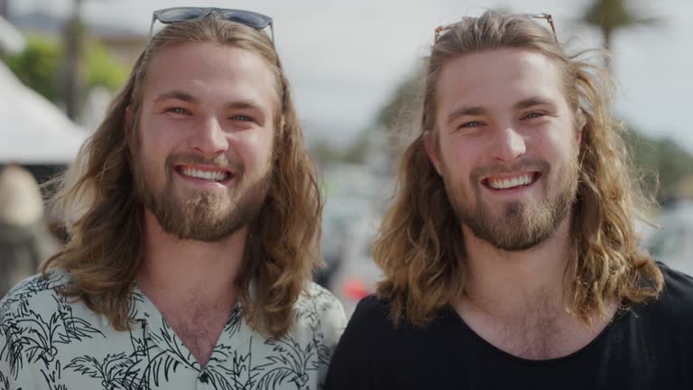 portrait of attractive twin brothers smiling happy on vacation enjoying summer travel in urban beachfront background