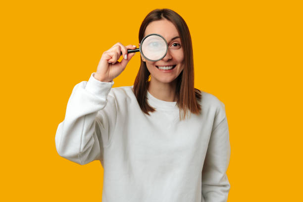 Wide smiling woman is looking through a magnifying glass at the camera. stock photo