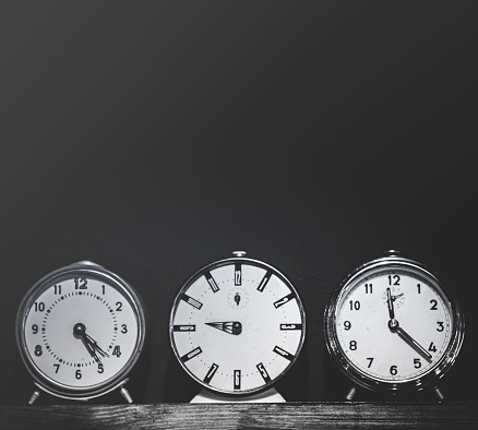 A black and white image of three classic circle-shaped analog clocks displayed on a shelf