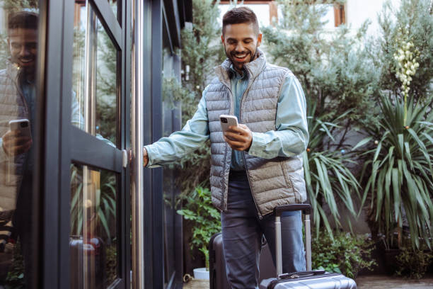 young man with suitcase using smart phone in front of the rented apartment - garden key imagens e fotografias de stock