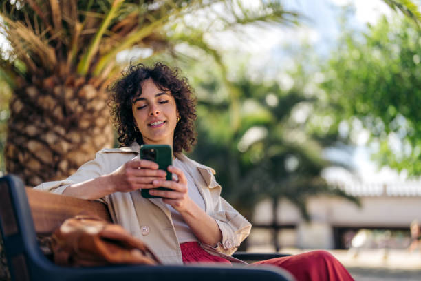 istock Smiling modern young woman using mobile phone technology while sitting on park bench 1490431347