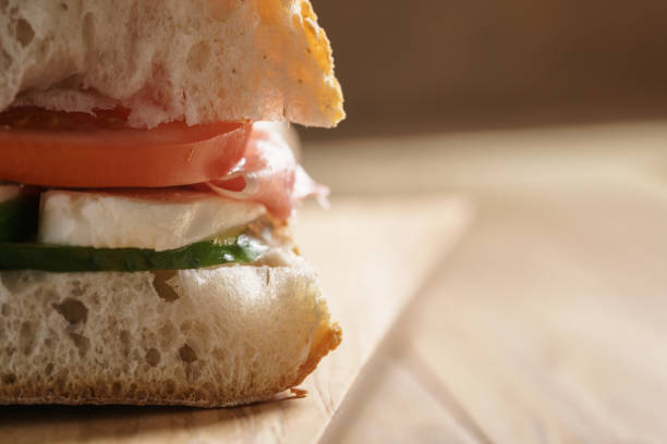 A close-up of a sliced Bacon, lettuce and tomato on white bread toasted with mayonnaise sitting on a piece of wax paper on a wooden cutting board
