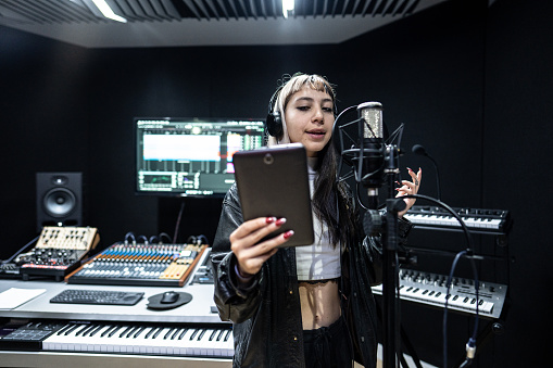 Singer young woman using digital tablet while sing in the recording studio