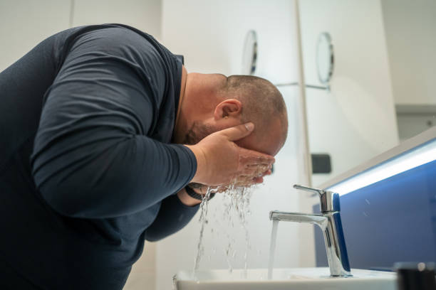 istock Overweight balded man washing face in bathroom at home under sink, side view. 1490439752