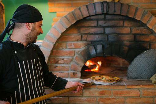 Pizza chef taking out fresh baked pizza from wooden oven