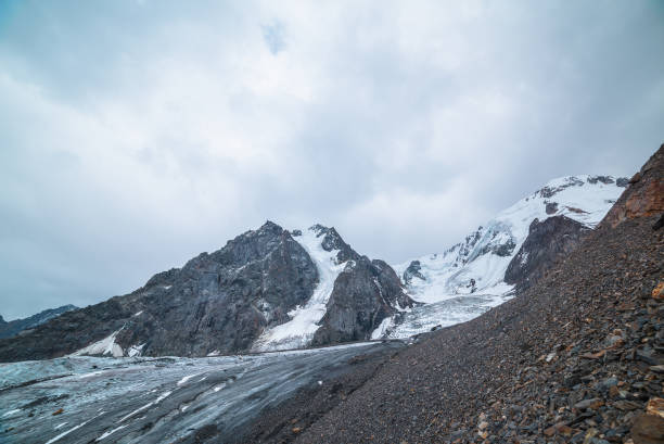 istock Dramatic landscape with glacier tongue and icefall on large snow mountain range with sharp rocky pinnacle under gray cloudy sky. Long glacier in high altitude. Gloomy scenery in mountains in overcast. 1490441242