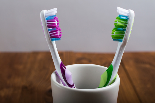Tooth protection. Healthcare concept. White ceramic cup with two toothbrushes on the wooden table.