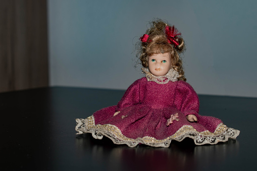 Portrait of collectible porcelain doll wearing period clothing with blond hair, headdress and blue eyes