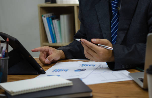 istock Businessperson reviewing documents with pen, analyzing data on graph report statistic and chart finance, budget, investment, accountant, diagram on desk. 1490446956