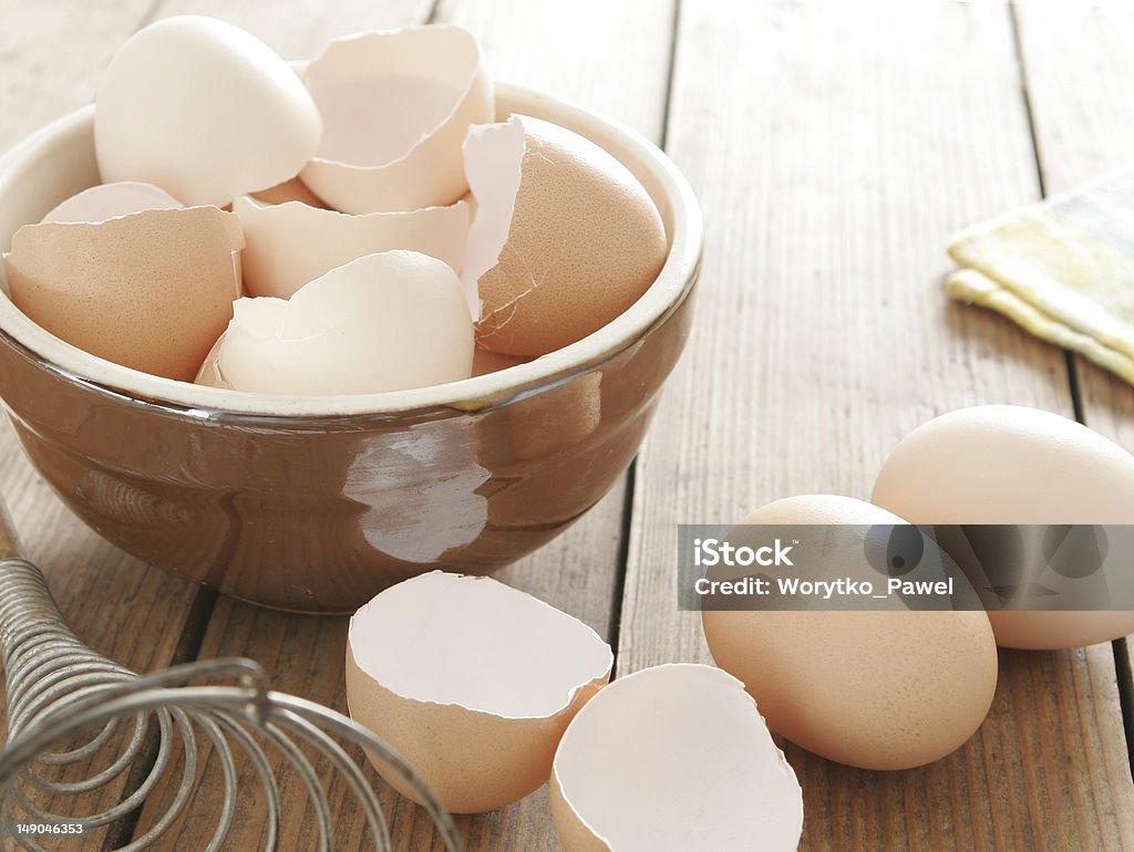 Egg shells in ceramic bowl Egg shells in ceramic bowl. Some eggs, egg beater and table cloth next to it. All on wooden table. Eggshell Stock Photo