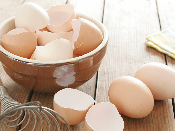 Egg shells in ceramic bowl Egg shells in ceramic bowl. Some eggs, egg beater and table cloth next to it. All on wooden table. eggshell stock pictures, royalty-free photos & images