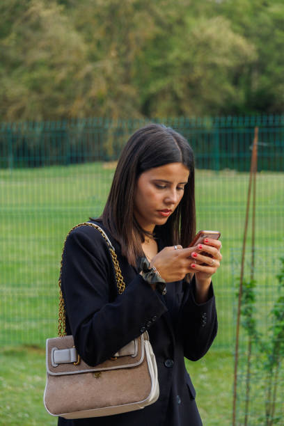 istock young model girl wearing make-up and using her cell phone with a handbag slung over her shoulder 1490463992
