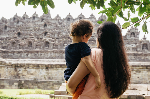 asian Chinese woman carrying her son walking on the grass with Borobudur temple in the background
