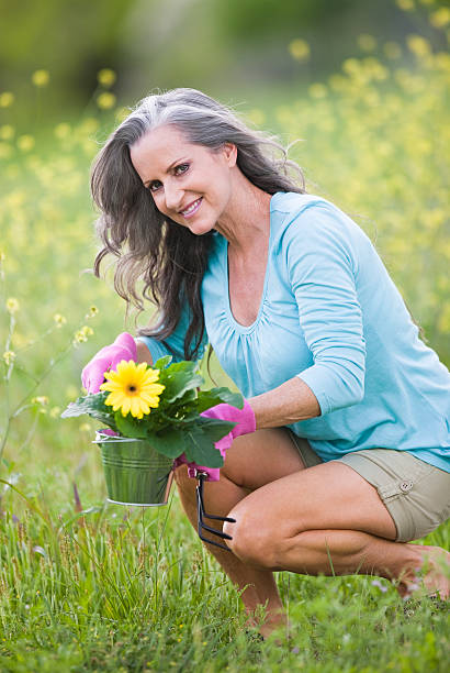 sênior mulher jardinagem em campo de flores silvestres - planting clothing gray hair human age - fotografias e filmes do acervo