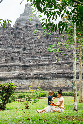 asian woman with her son sitting  on the grass with Borobudur temple in the background