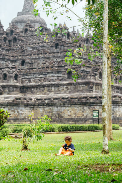 a kid walking on the grass with borobudur temple in the background