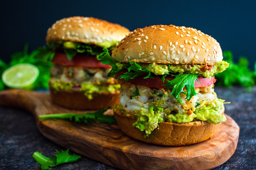 Seafood hamburger sandwiches made topped with guacamole and sliced tomato