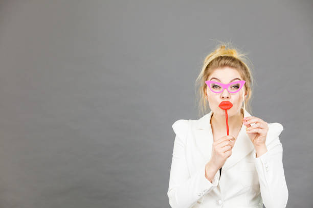 Happy elegant woman holding carnival accessoies on stick having fun at work wearing white office jacket
