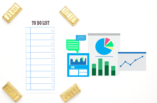 Flatlay picture of to do list paper with miniature gold bar with business graph on white background. To do list in gold investment and trading.