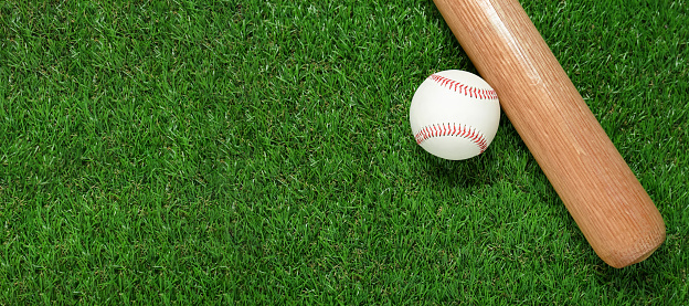 Wooden baseball bat and ball on green grass, flat lay. Sports equipment