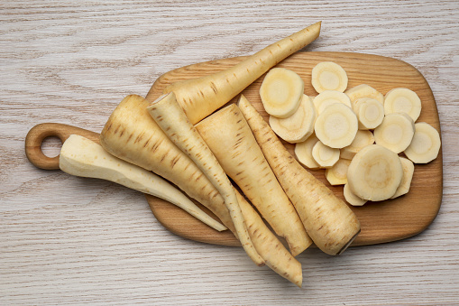 Whole and cut fresh ripe parsnips on white wooden table, top view