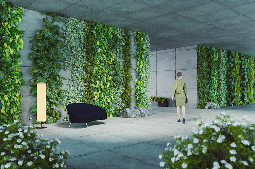 Businesswoman walking in office corridor full of vertical plants. 3D generated image.