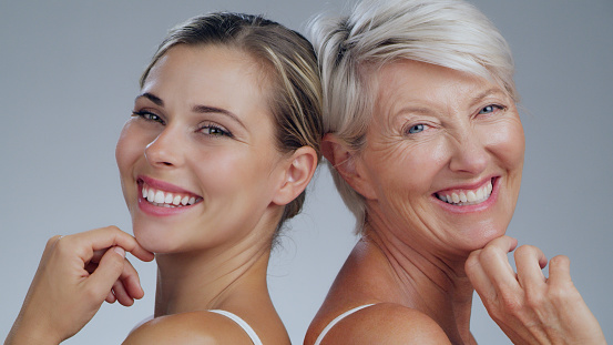 Portrait, beauty or skin with a woman and daughter in studio on a gray background for antiaging treatment. Skincare, smile or happy with a young and old person posing together for natural cosmetics