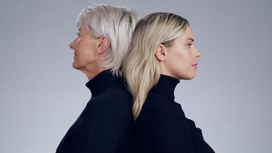 Serious, fashion and profile of mother and daughter isolated on a grey studio background. Back to back and strong senior mom with a girl looking stylish, fashionable on a backdrop