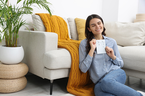 Young woman with greeting card on floor in living room