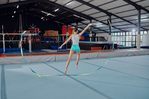 Training, gymnastics and dance with ribbon and woman in gym for sports, fitness and wellness. Motivation, exercise and health with gymnast athlete dancing for performance, competition and energy