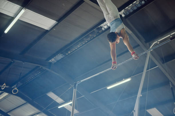 Gymnastics, exercise and workout with a man gymnast training on a bar in a gym or studio. Fitness, sports and health with a male athlete practicing on high bars for a competition
