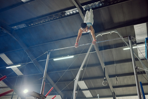 Gymnastics, exercise and workout with a man gymnast training on a bar in a gym or studio. Fitness, sports and health with a male athlete practicing on high bars for a competition