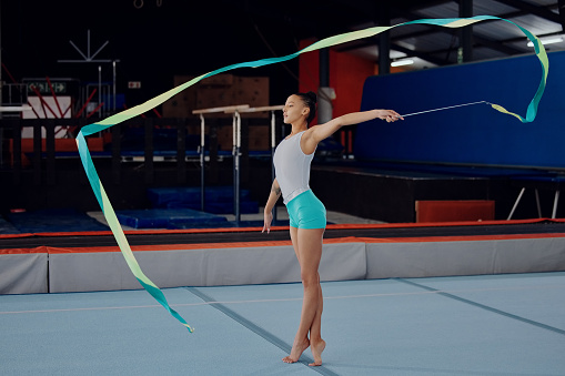 Training, gymnastics and dance with ribbon and woman in gym for sports, fitness and wellness. Motivation, exercise and health with gymnast athlete dancing for performance, competition and energy
