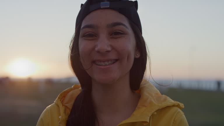 close up portrait of awkward teenage girl smiling cheerful looking at camera wearing braces enjoying park at sunset