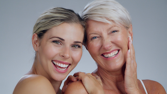 Portrait, beauty or funny with a mother and daughter in studio on a gray background for antiaging treatment. Skincare, smile or happy with a young and old person posing together for natural cosmetics