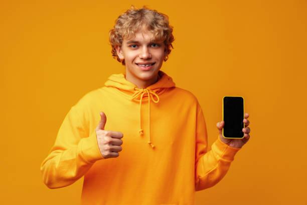 istock Young smiling man holding smartphone with blank device screen against yellow background 1490490203