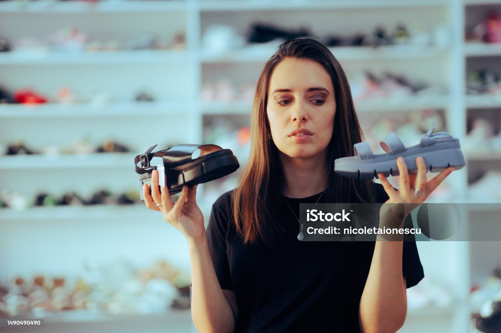 Woman in Shoes Store Comparing Two Comfortable Summer Sandals Indecisive customer trying to make an ethical decision Sandal Stock Photo