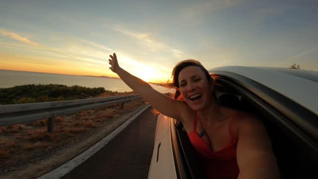 PORTRAIT, LENS FLARE: A cute lady smiles through window of a car driving by sea