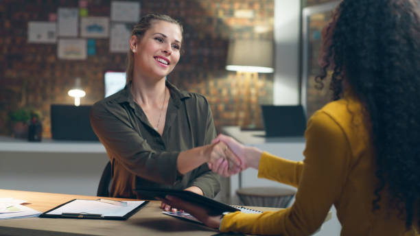 istock Creative business people, handshake and hiring at night for recruitment, interview or greeting at office. Happy women shaking hands working late for deal, b2b or partnership and meeting for startup 1490497966