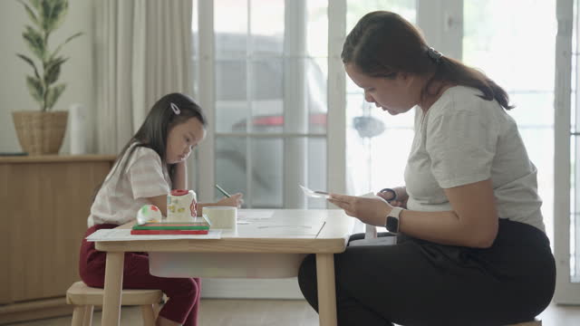 Mother spending time with her little daughter playing together with coloring activity and papercut