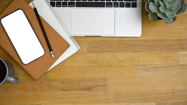 Workspace top view with laptop computer, smartphone white screen mockup, pencil, books, coffee cup, decor plant and copy space on wooden tabletop.
