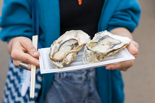 A close-up of a woman's hands holding a food market favorite, a tray of Oysters ready to eat from a street food market.