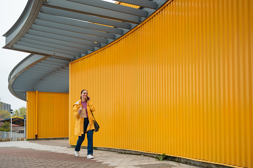 Latin woman outdoors wearing a yellow rain coat talking on the phone in a minimalist style photography