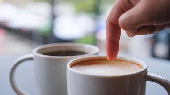 Closeup image of a finger pointing at a cup of hot coffee on the table