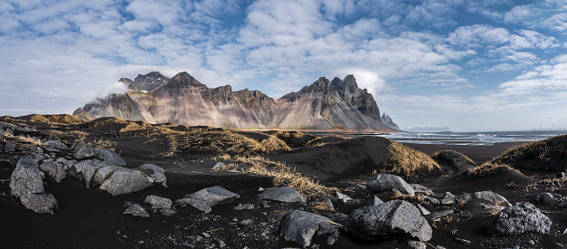 Panoramic view of the otherworldly Vestrahorn mountains as well as the black beach and sand dunes on the Stokksness peninsula on a sunny day in spring, close to Höfn, Iceland, April 2023.