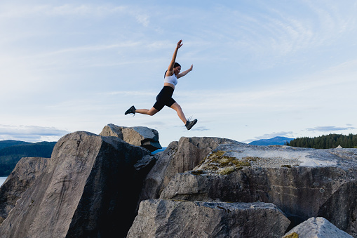 Female hiker jumps from rock to rock with the sky as the background. Shot in the Columbia River Gorge in Oregon.