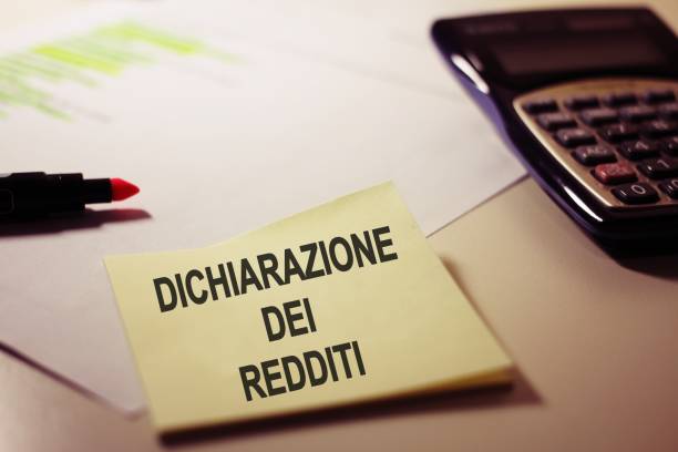 local de trabalho com uma nota de post it com o texto dichiarazione dei redditi traduzindo em italiano como declaração de rendimentos , conceito de pagamento de imposto . - incomes - fotografias e filmes do acervo