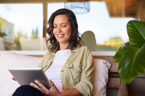 Mid-shot portrait of smiling woman reading on digital tablet while sitting in her living room