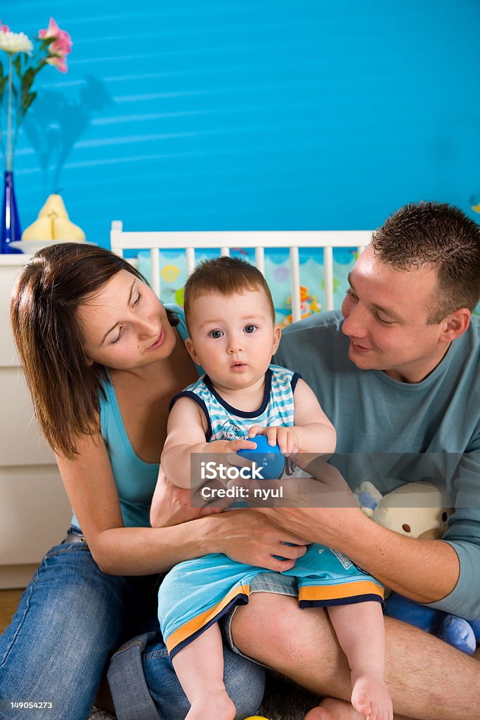 Happy family at home Portrait of happy family at home. Baby boy ( 1 year old ) and young parents father and mother sitting on floor and playing together at children's room, smiling. Click here for more baby photos: 25-29 Years Stock Photo
