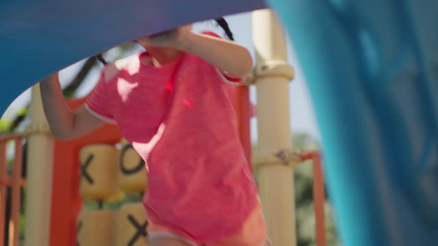 Cute cheerful little 4-year-old Asian girl climbing on a colorful slider at playground. Active little girl playing on outdoor playground. Healthy summer activity for child.